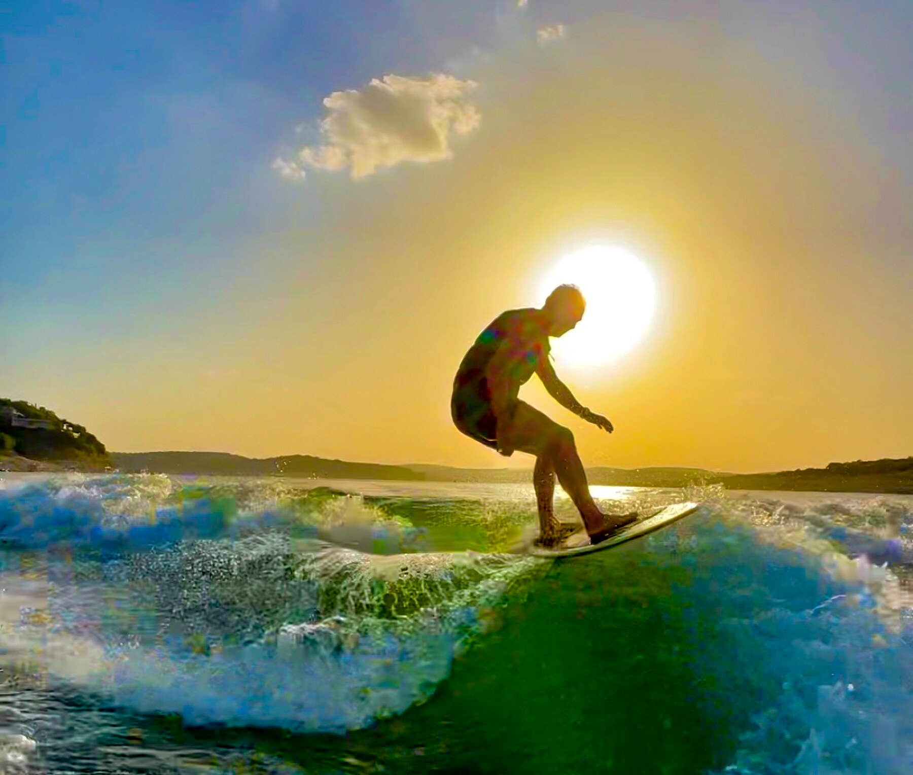 A wakesurfer riding a sunlit wave on Lake Travis